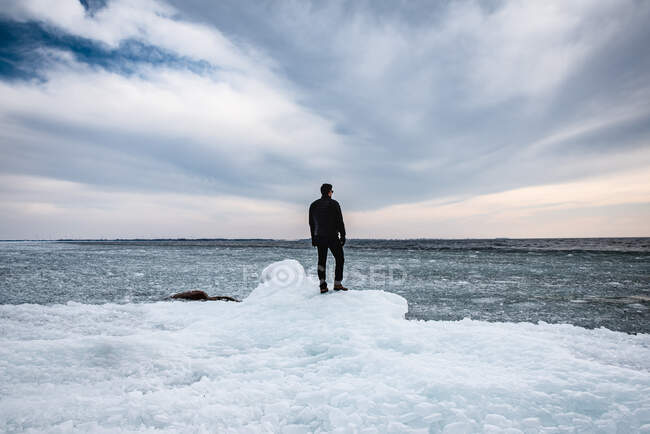Человек, стоящий на ледяной береговой линии озера, глядя вдаль. — стоковое фото
