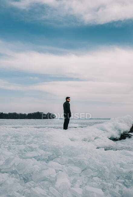 Uomo in piedi su una costa ghiacciata di un lago guardando in lontananza. — Foto stock