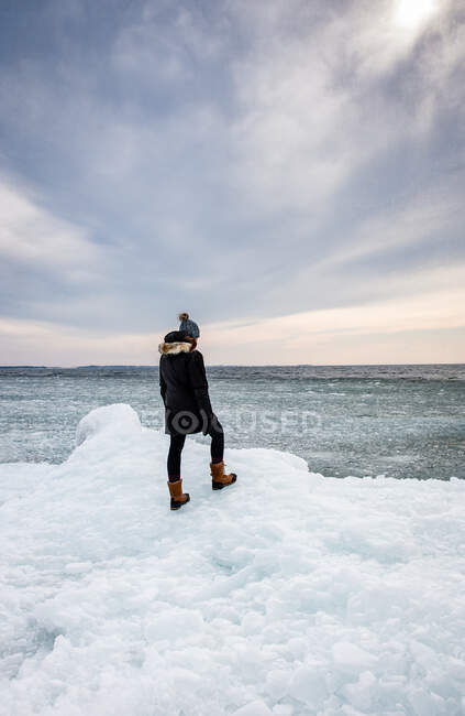 Женщина, стоящая на ледяной береговой линии озера, глядя вдаль. — стоковое фото