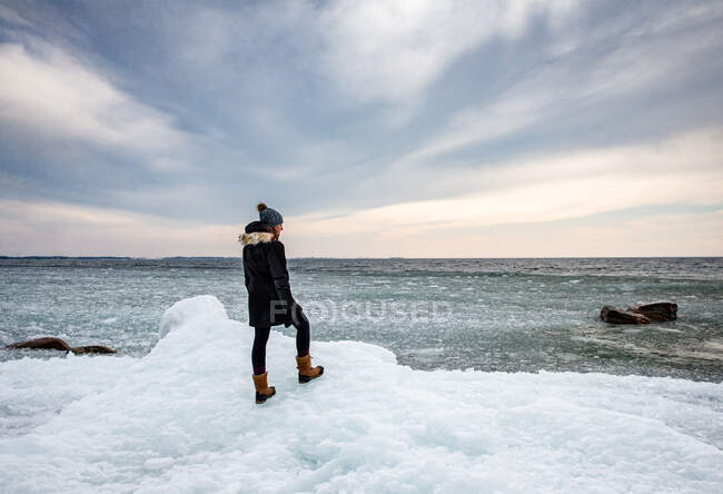 Donna in piedi sulla costa ghiacciata di un lago guardando in lontananza. — Foto stock