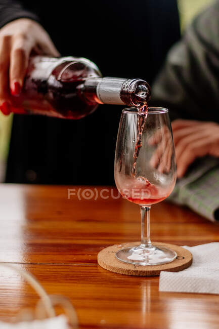 Echar vino en una copa sobre una mesa de madera - foto de stock