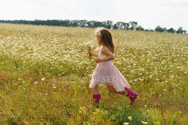 Little girl running in a flower field in the summer. — Stock Photo