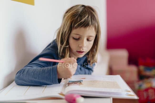 Симпатичная девушка, смотрящая на свою домашнюю работу — стоковое фото