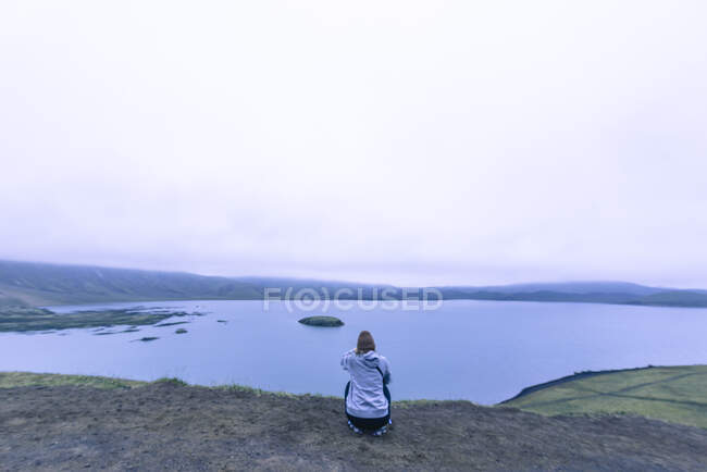 Femme assise en train de photographier un lac dans les hautes terres islandaises au coucher du soleil — Photo de stock