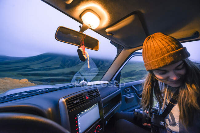 Frau mit Kamera und Hut sitzt im Auto und blickt auf den Sonnenuntergang — Stockfoto
