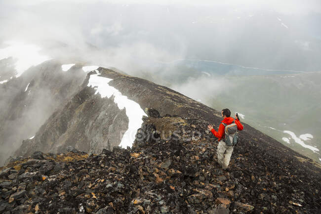 Un homme descend une crête à travers les nuages sous le sommet de Cooper Mountain, péninsule de Kenai, Alaska. — Photo de stock