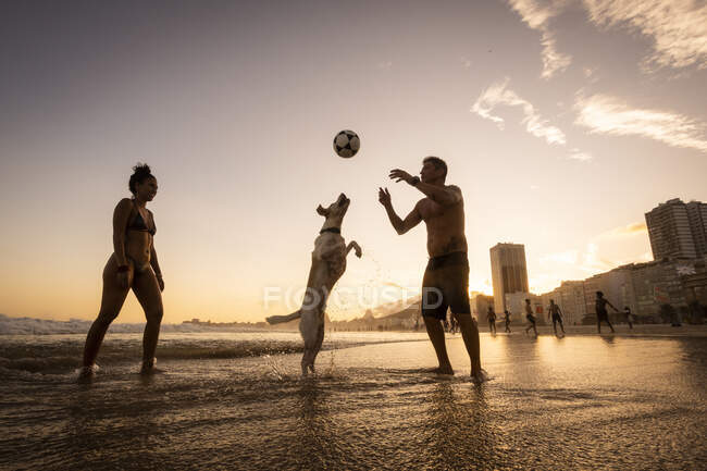 Casal jogando futebol com cão na frente da água em Copacabana Beach — Fotografia de Stock