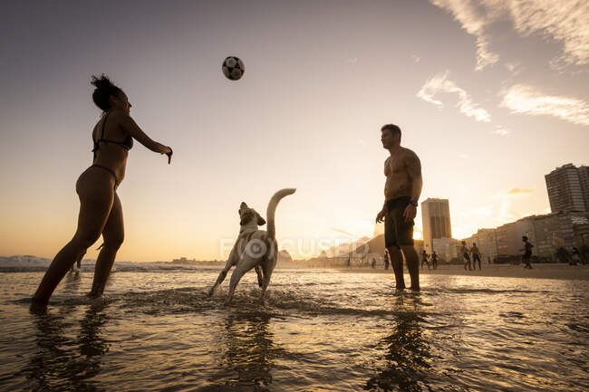 Coppia che gioca a calcio con cane sul lungomare a Copacabana Beach — Foto stock