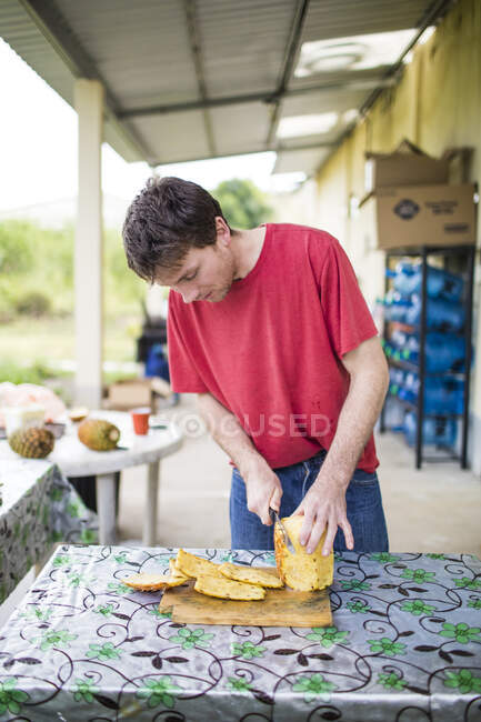 Jeune homme coupant de l'ananas frais et bio sur une planche à découper en bois. — Photo de stock