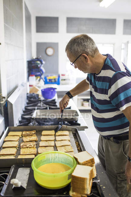 Літній чоловік готує французький тост на промисловій кухні . — стокове фото