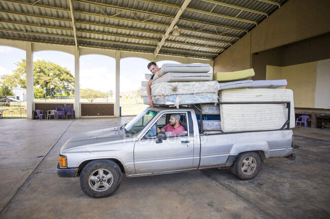 Due uomini che cavalcano su camion caricato aiutano a spostare materassi in orfanotrofio. — Foto stock