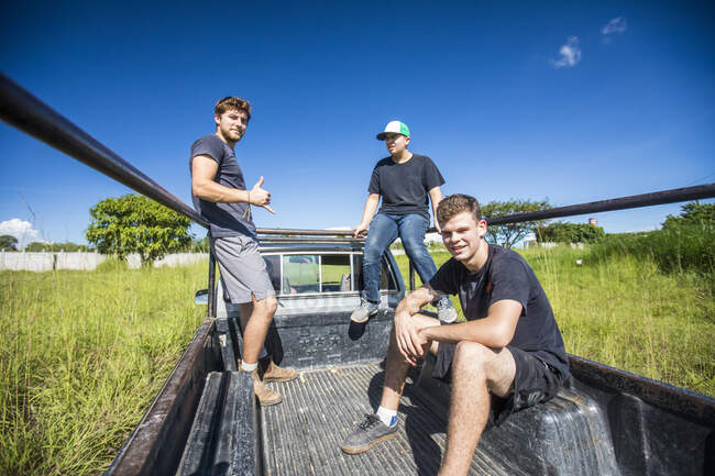 Трое молодых людей едут через поле на заднем сиденье грузовика 4х4 — стоковое фото
