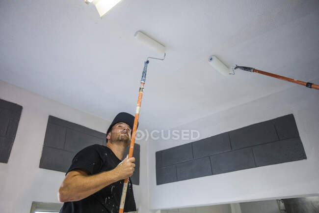 Painter uses roller to paint ceiling white. — Stock Photo
