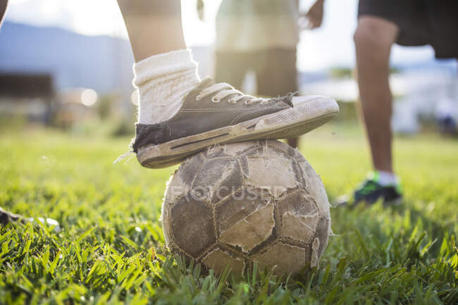 Joueur de football (football) place vieille chaussure sur le ballon de football déchiré — Photo de stock