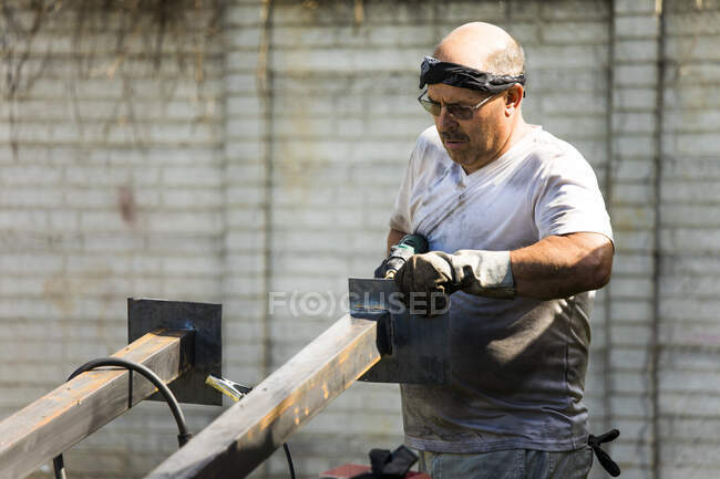 Metal worker fabricating metal posts in outdoor workshop. — Stock Photo