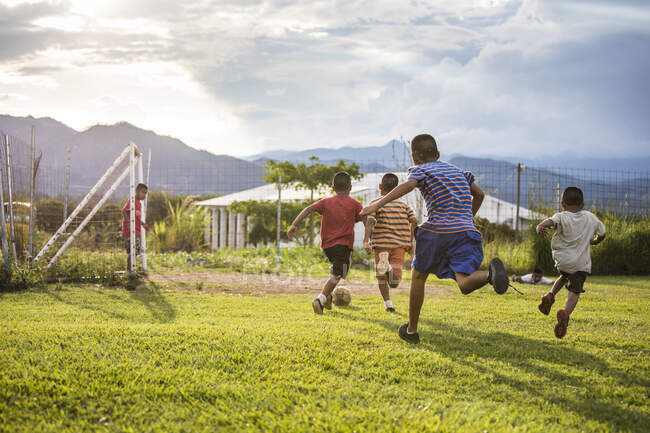 Grupo de amigos jogando futebol no campo de grama antes do pôr do sol. — Fotografia de Stock