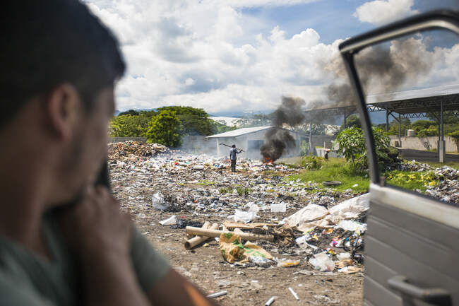 View from vehicle of worker at dump burning garbage. — Stock Photo