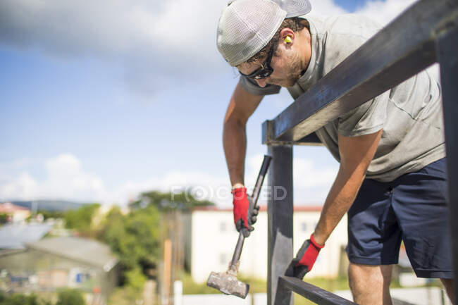 Construction worker using hammer to build steel railing on roof. — Stock Photo