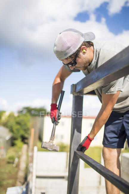 Construction worker using hammer to build steel railing on roof. — Stock Photo