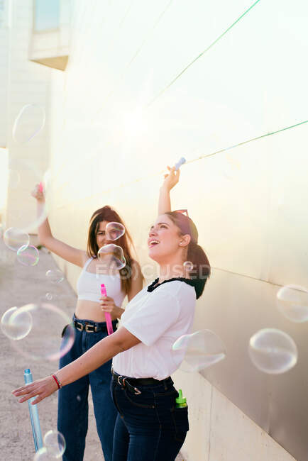 Дві молоді дівчата розважаються під час заходу сонця, роблячи мильні бульбашки — стокове фото
