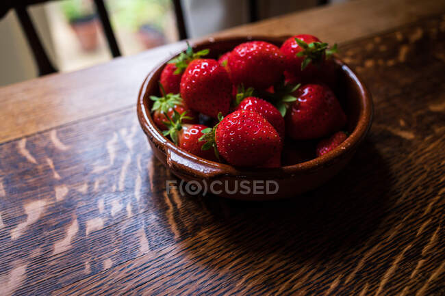 Tazón de fresas en una mesa de madera - foto de stock