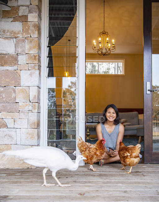 Donna seduta sulla porta di casa e nutrire gli uccelli domestici — Foto stock