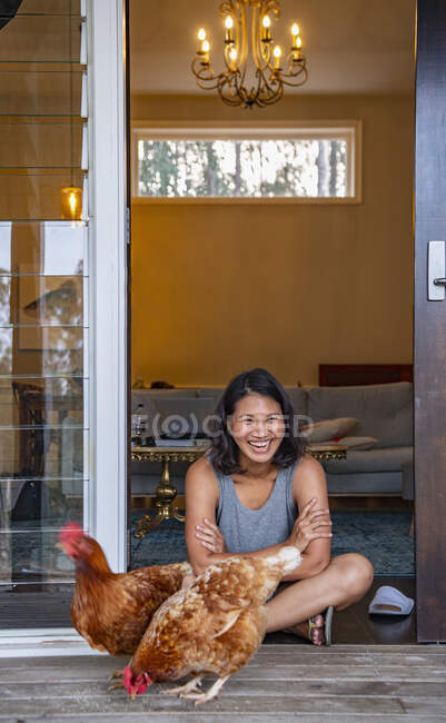 Woman sitting in the doorway of house and feeding the domestic birds — Stock Photo