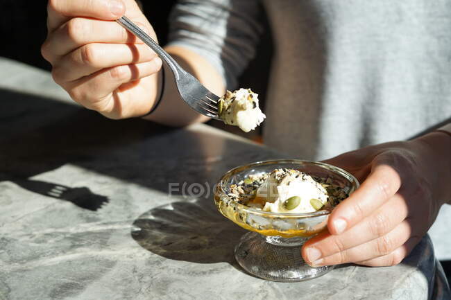 Mujer joven sosteniendo una cucharada de yogur, semillas y miel a la luz del sol.. - foto de stock