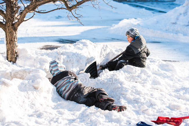 Dois meninos construindo fortes de neve com pás em um dia ensolarado de inverno. — Fotografia de Stock