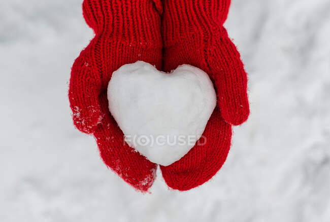Gros plan de deux mains dans des mitaines rouges tenant boule de neige en forme de coeur. — Photo de stock