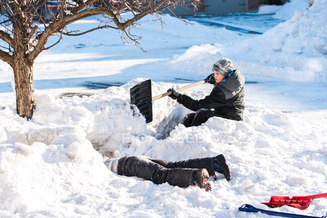Due ragazzi costruiscono fortezze di neve con pale in una giornata invernale soleggiata. — Foto stock