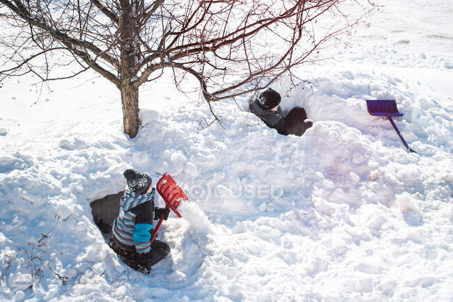 Dos chicos construyendo fuertes de nieve con palas en un día soleado de invierno. - foto de stock