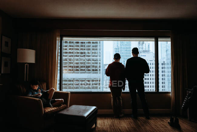 Man and boy looking out window at tall buildings of the city outside. — Stock Photo
