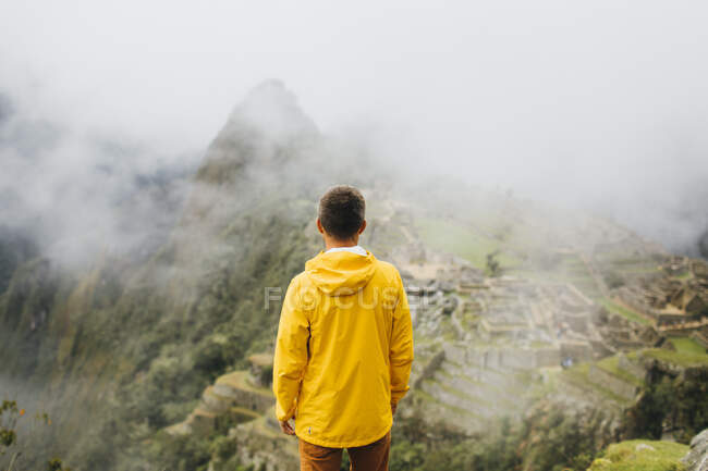 Человек в жёлтой куртке стоит рядом с руинами Мачу-Пикчу, Перу — стоковое фото