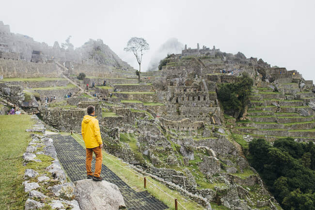 Un uomo in giacca gialla è in piedi vicino alle rovine di Machu Picchu, Perù — Foto stock