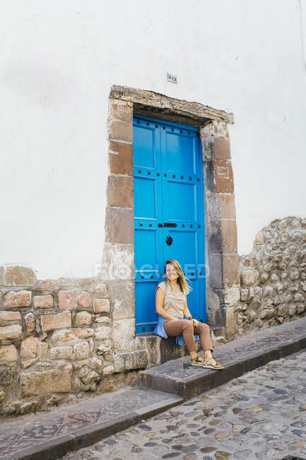 Una giovane donna è seduta vicino a una vecchia porta blu a Cusco, Perù — Foto stock