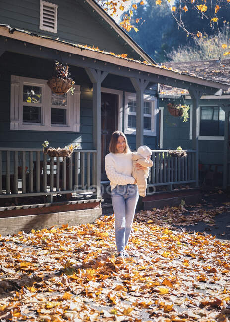 Una donna con un bambino è in piedi vicino a una casa su foglie gialle — Foto stock