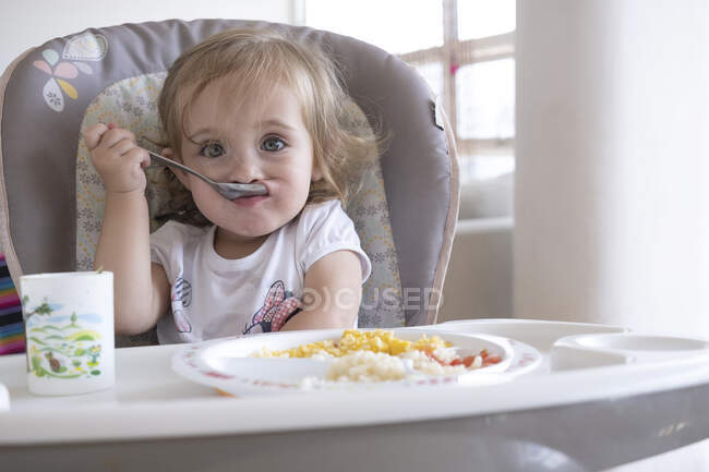 Маленька дівчинка їсть сама в кріслі за столом . — стокове фото