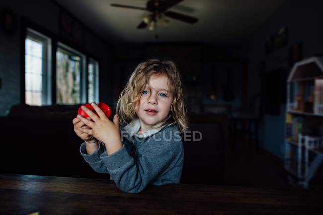 Niño con el pelo largo y rubio y los ojos azules sentados en una mesa - foto de stock