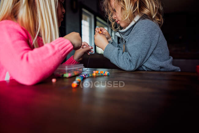 Niño y niña haciendo collar de cuentas dentro de una mesa - foto de stock
