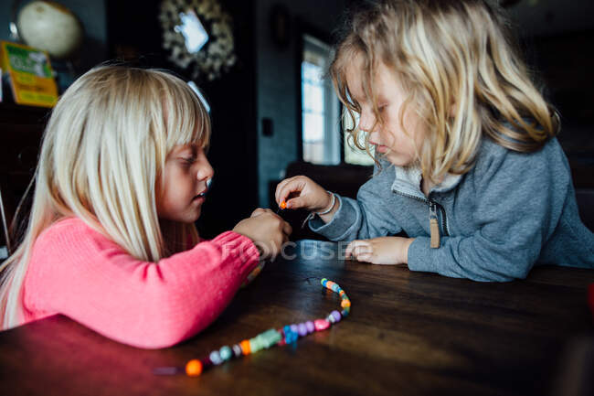 Little boy and girl making bead necklace at table during the day — Stock Photo