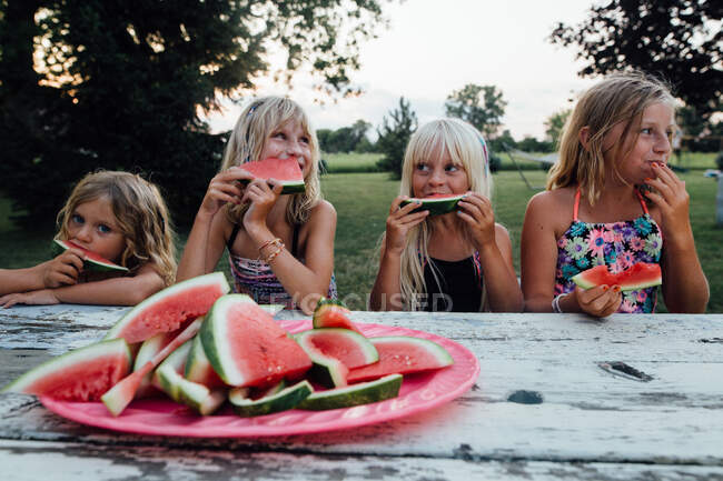 Siblings sitting at picnic table outside eating watermelon in summer — Stock Photo