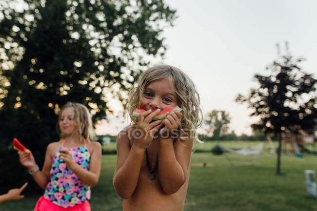 Jeune garçon aux cheveux longs mangeant de la pastèque à l'extérieur en été — Photo de stock