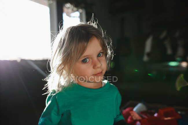 Маленький хлопчик з довгим волоссям дивиться на камеру з соняшником з вікна — стокове фото