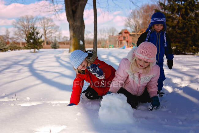 Діти грають назовні взимку роблячи снігову кулю — стокове фото