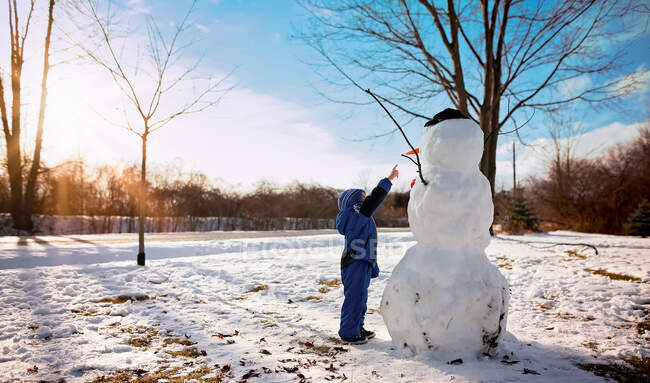 Маленький хлопчик вказує сніговику в сонячний день — стокове фото