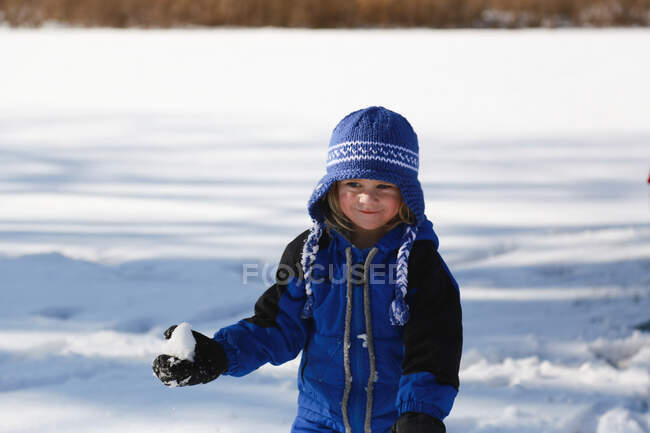 Kleiner Junge hält Schneeball draußen im blauen Schneeanzug — Stockfoto