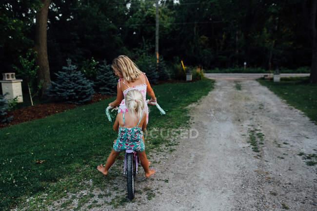 Two girls riding a bike down a driveway in the summer — Stock Photo