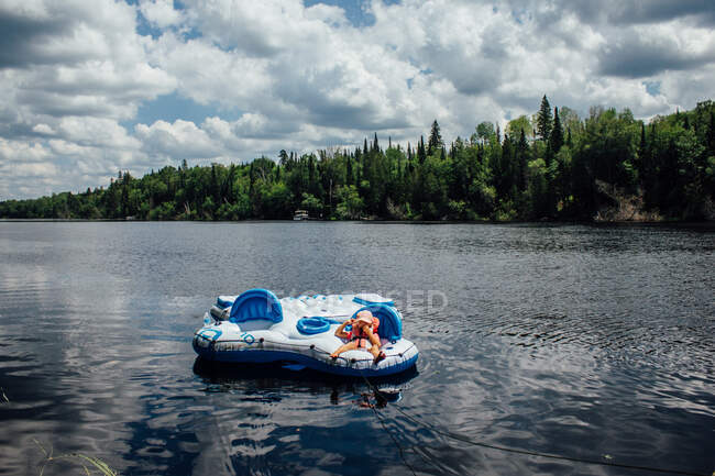 Young child laying on floating raft on river in northern ontario — Stock Photo