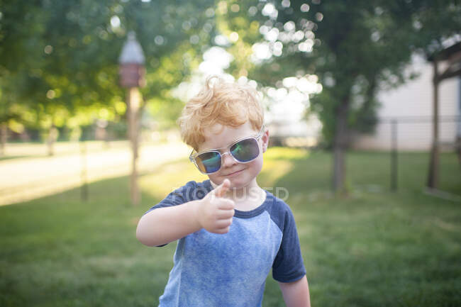 Giovane ragazzo che dà un pollice con gli occhiali da sole in piedi in cortile — Foto stock